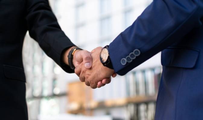 Geschäftspartner in Anzügen geben sich vor einem modernen Gebäude die Hand – Symbol für starke Vertriebspartnerschaft der SDH-Immobilien GmbH & Co. KG.